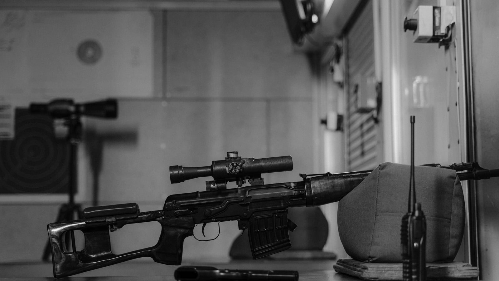 Scoped rifle resting on a shooting bag (bean bag), indoor firing line, round target in the background