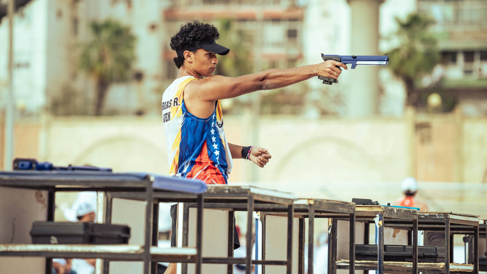 Sport shooter with a pistol, arm extended and confident posture, at an outdoor precision shooting competition