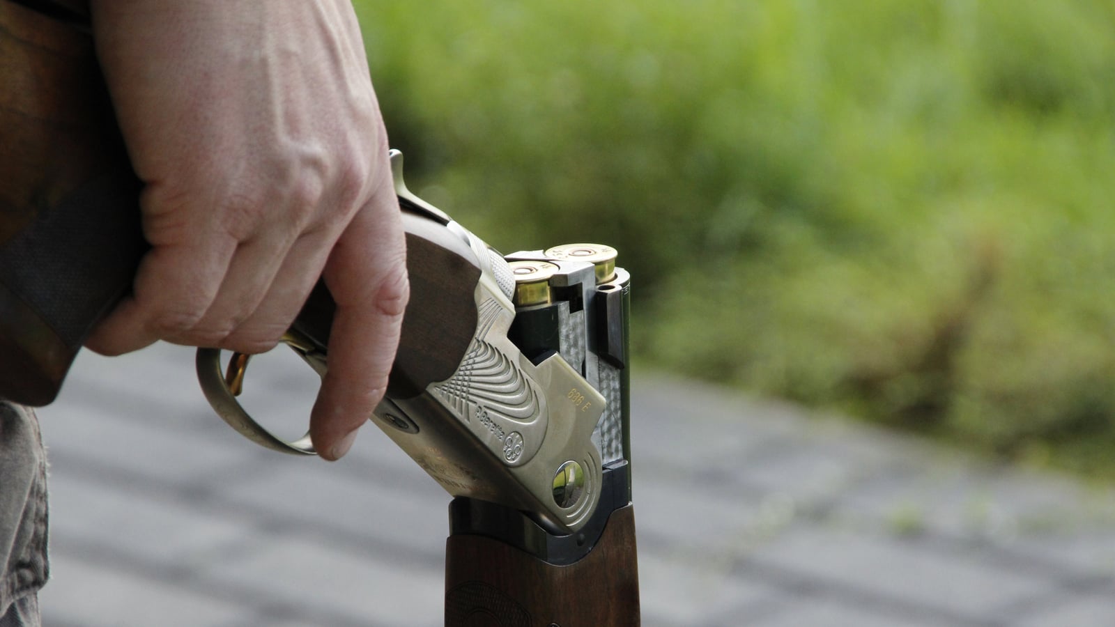 Break-action shotgun open, two shells visible in the chambers, held in hand after a shooting session