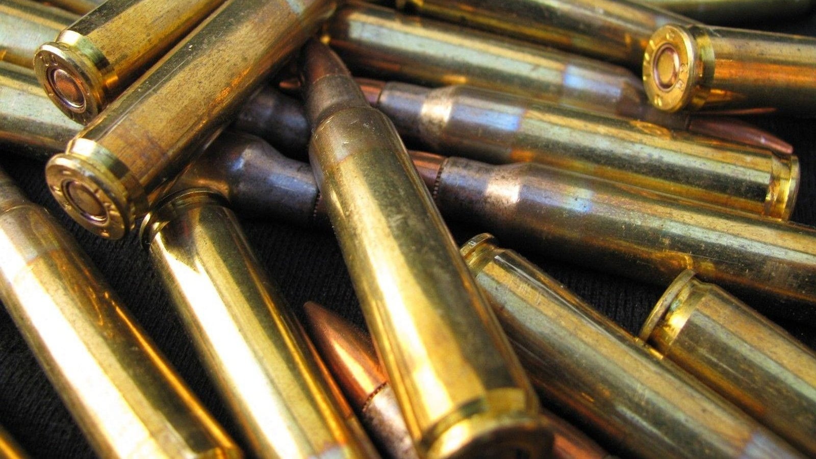 Close-up of a pile of brass rifle cartridges against a dark background