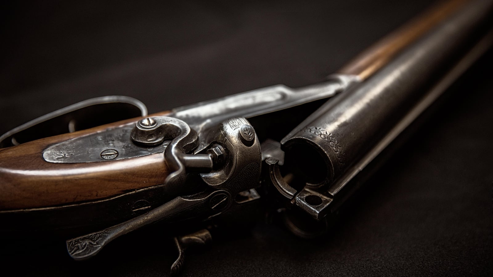 Close-up on the mechanism and open barrels of an old black powder gun resting on a dark surface