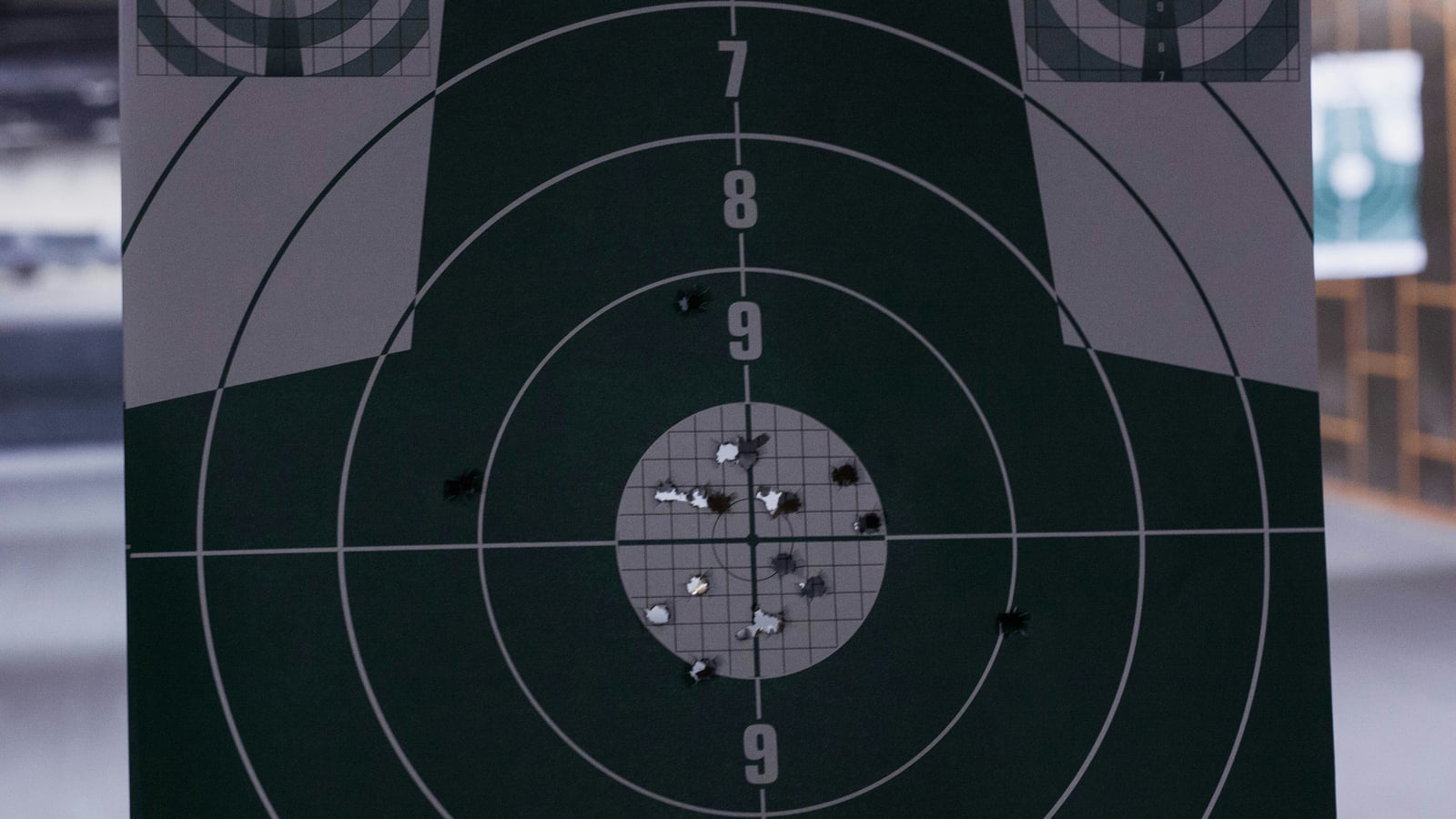Close-up of a 10-meter pistol target with numbered rings and a shot grouping in the center, indoor shooting range