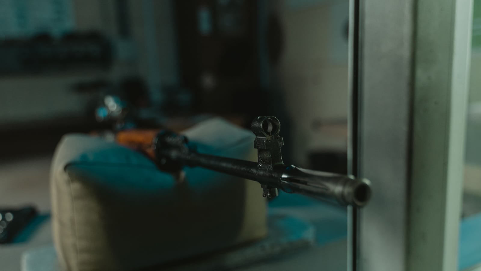Precision rifle resting on a rest, barrel pointed toward a blurred target at the far end of an empty, silent shooting range