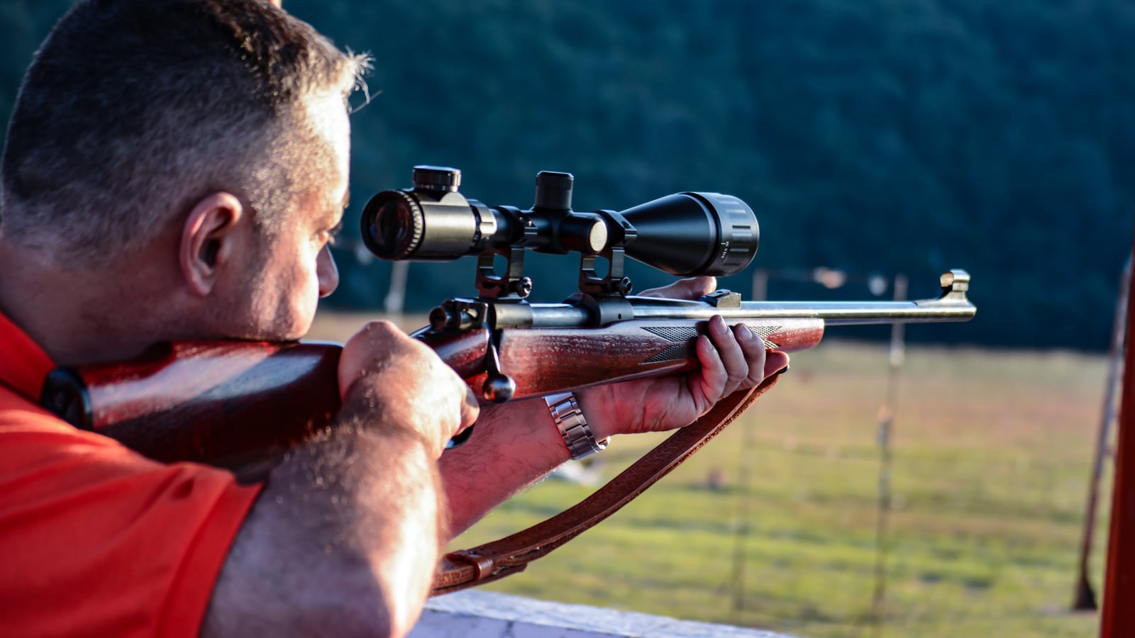 Close-up profile of a shooter's focused face aiming through a rifle scope on an outdoor range