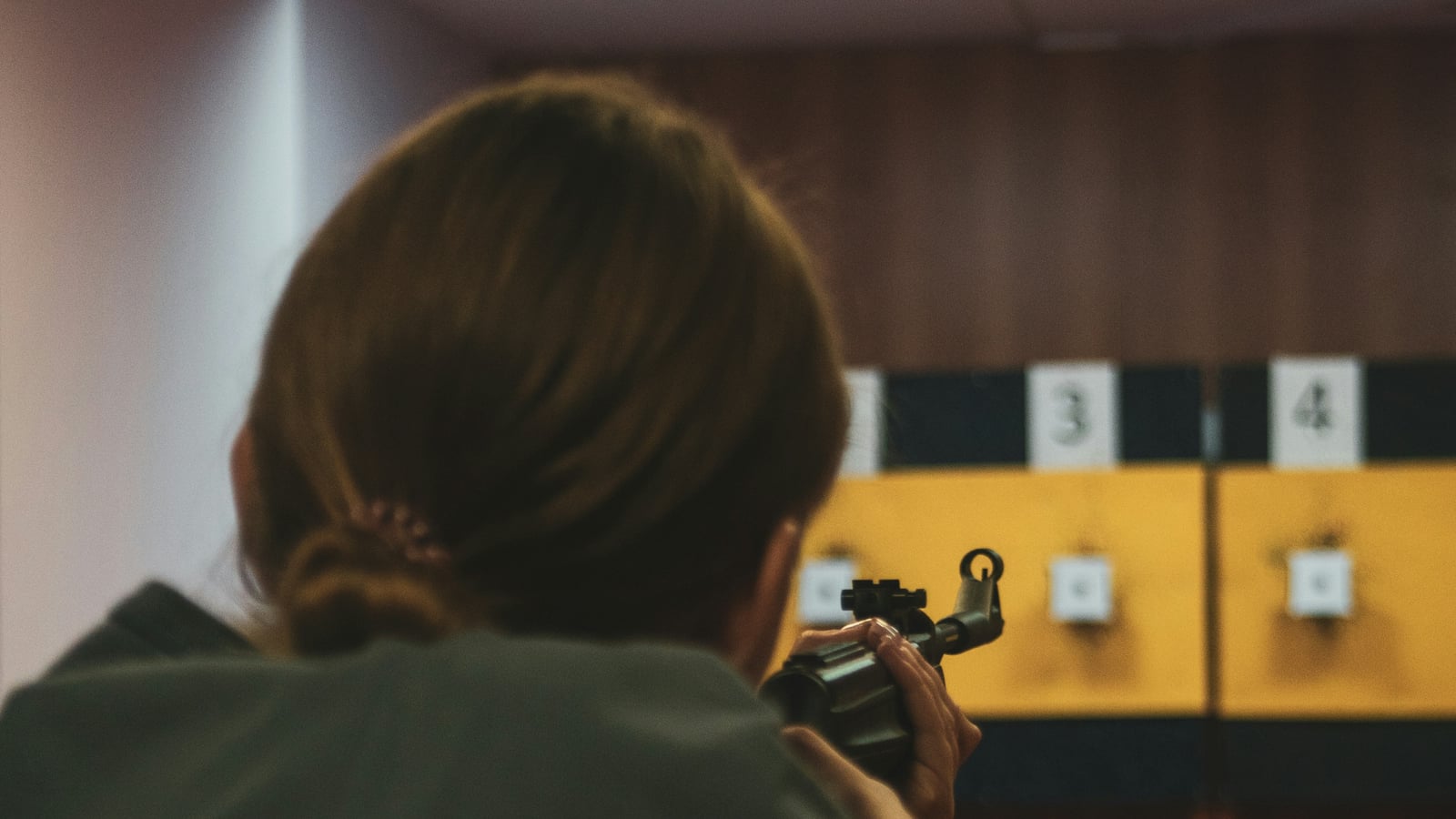 Female shooter aiming a pistol at targets on numbered firing points in a competition range
