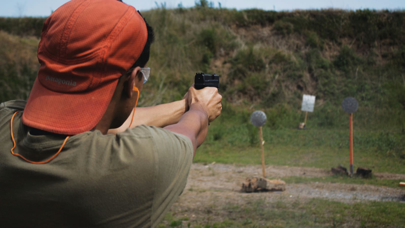 Pistol shooter aiming at round steel plates at an outdoor shooting range, a casing flying out mid-ejection