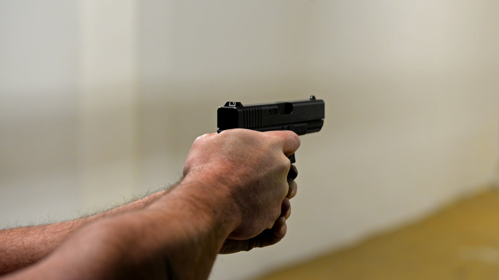 Hand holding a pistol mid-trigger-pull on an indoor firing line, finger on the trigger, illustrating the moment of the second shot