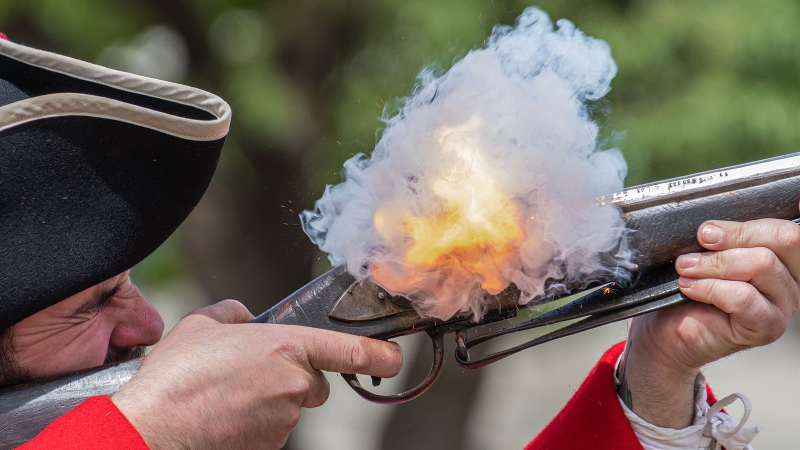 Reenactor in period costume firing a black powder musket, smoke plume and muzzle flash