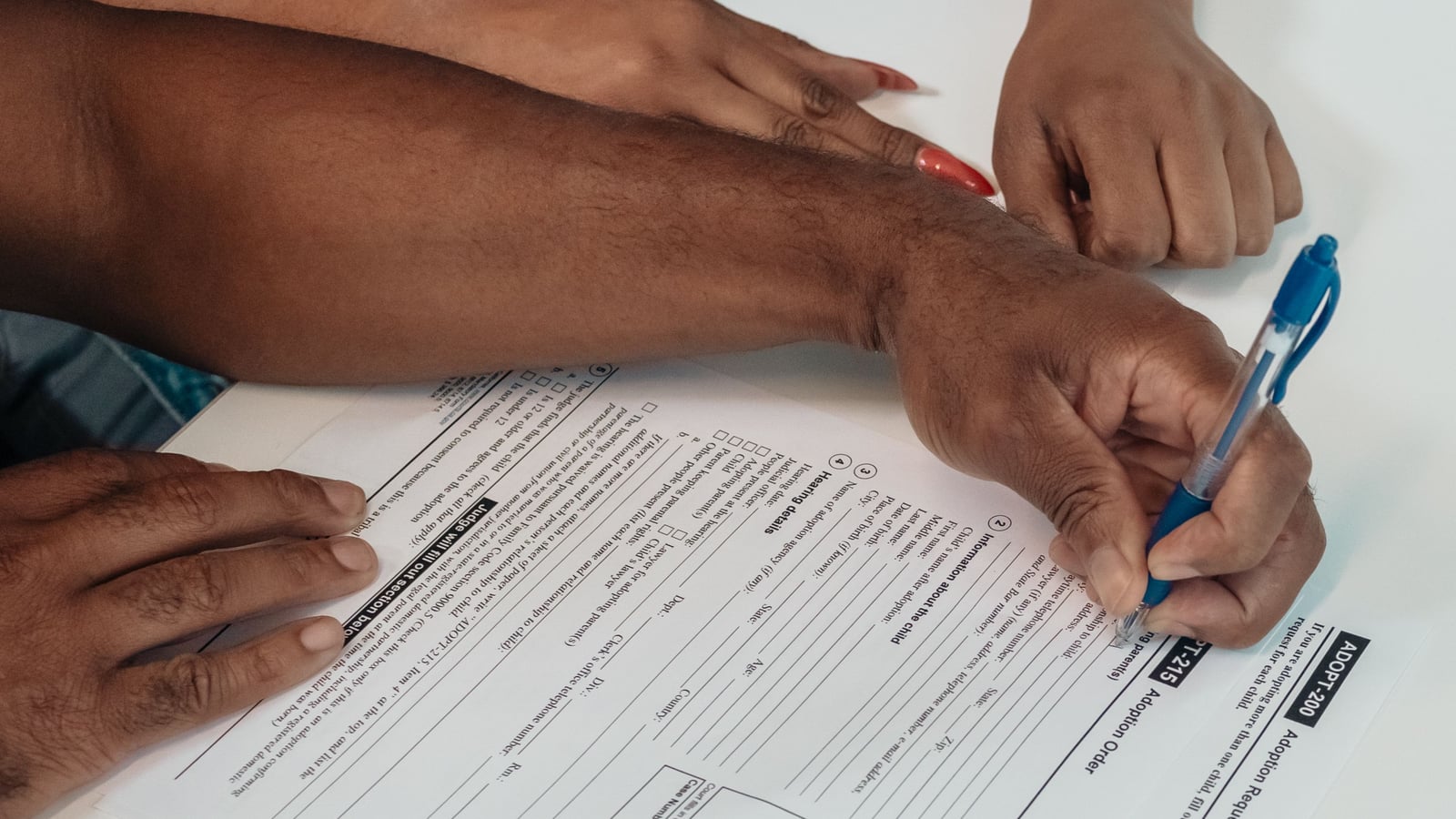 Close-up of two hands filling out and signing an official registration form together