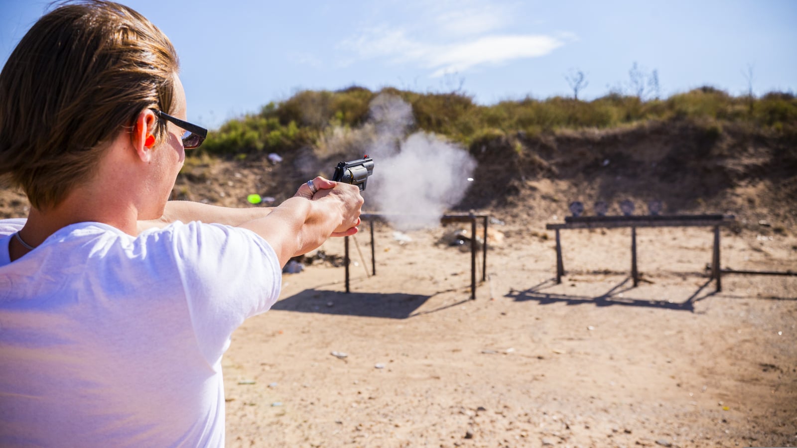 Shooter in action at an outdoor range, revolver in hand and smoke at the muzzle right after the shot